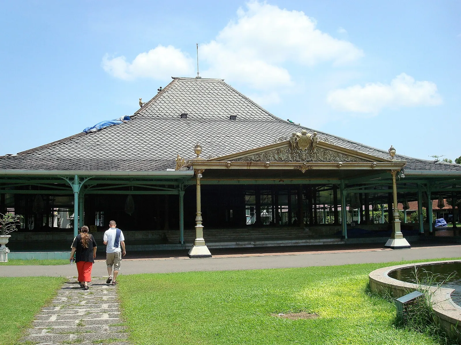 Two visitors walking towards the large open pendopo hall of Pura Mangkunegaran in Solo