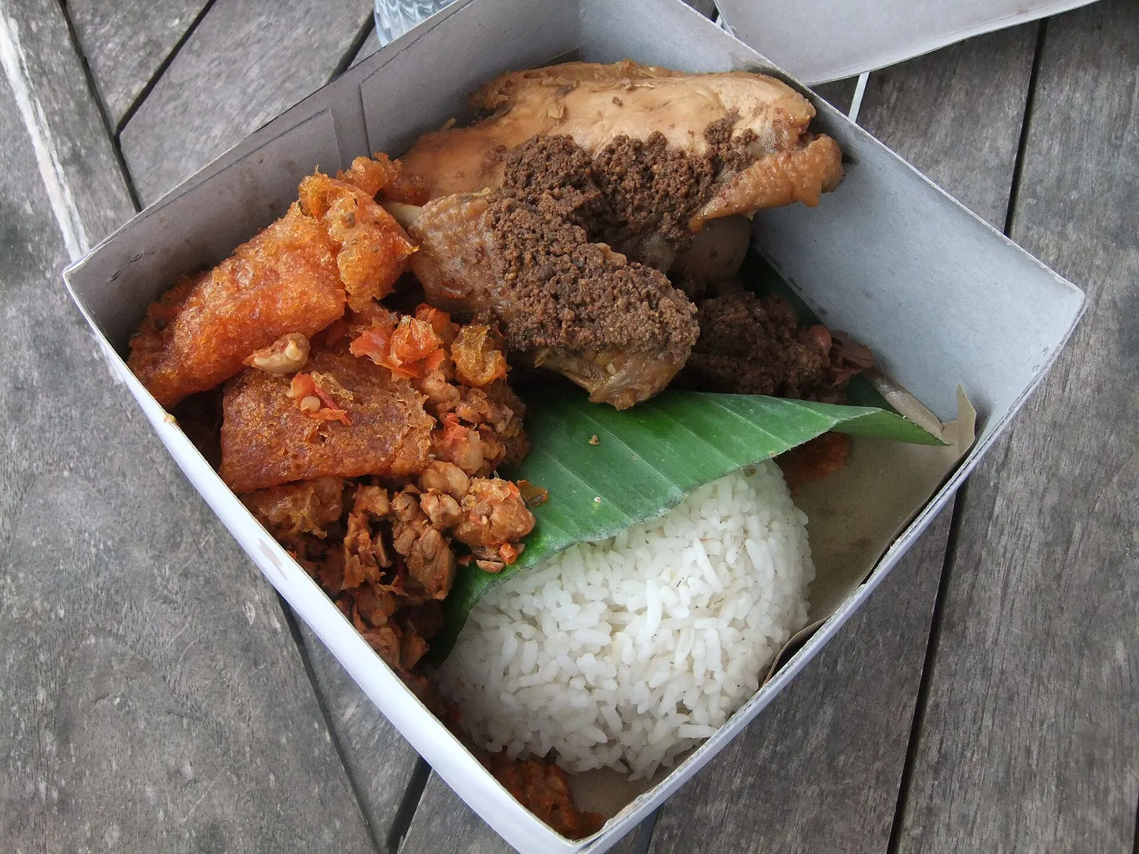 A boxed meal of gudeg with rice, chicken, krecek and tempe on a banana leaf