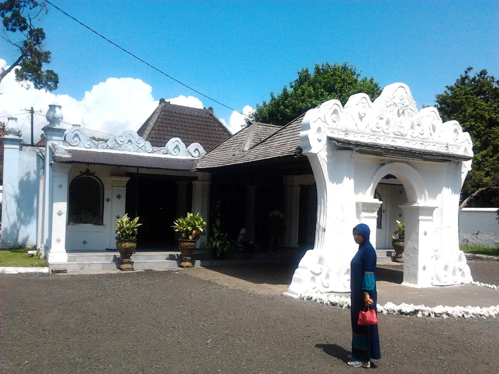 White-walled pavilions and the carved split gate of Keraton Kasepuhan under a blue sky in Cirebon
