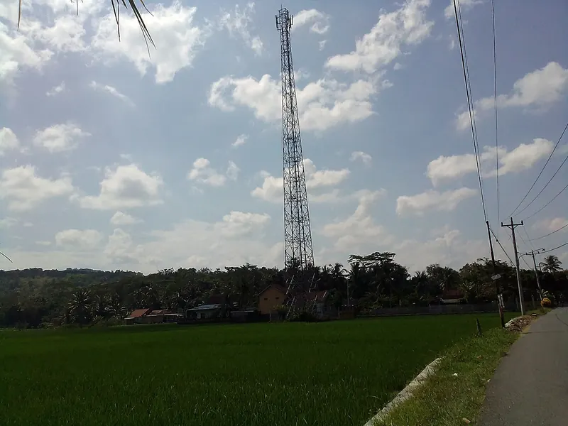 Telkomsel mobile phone tower rising above green rice fields under a blue sky in Karangtanjung, Kebumen, Central Java
