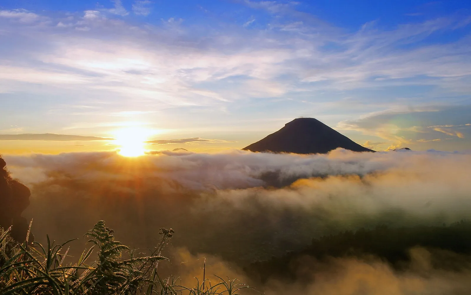 Sun rising over a sea of cloud with a volcanic cone on the horizon, seen from Sikunir Hill, Dieng Plateau