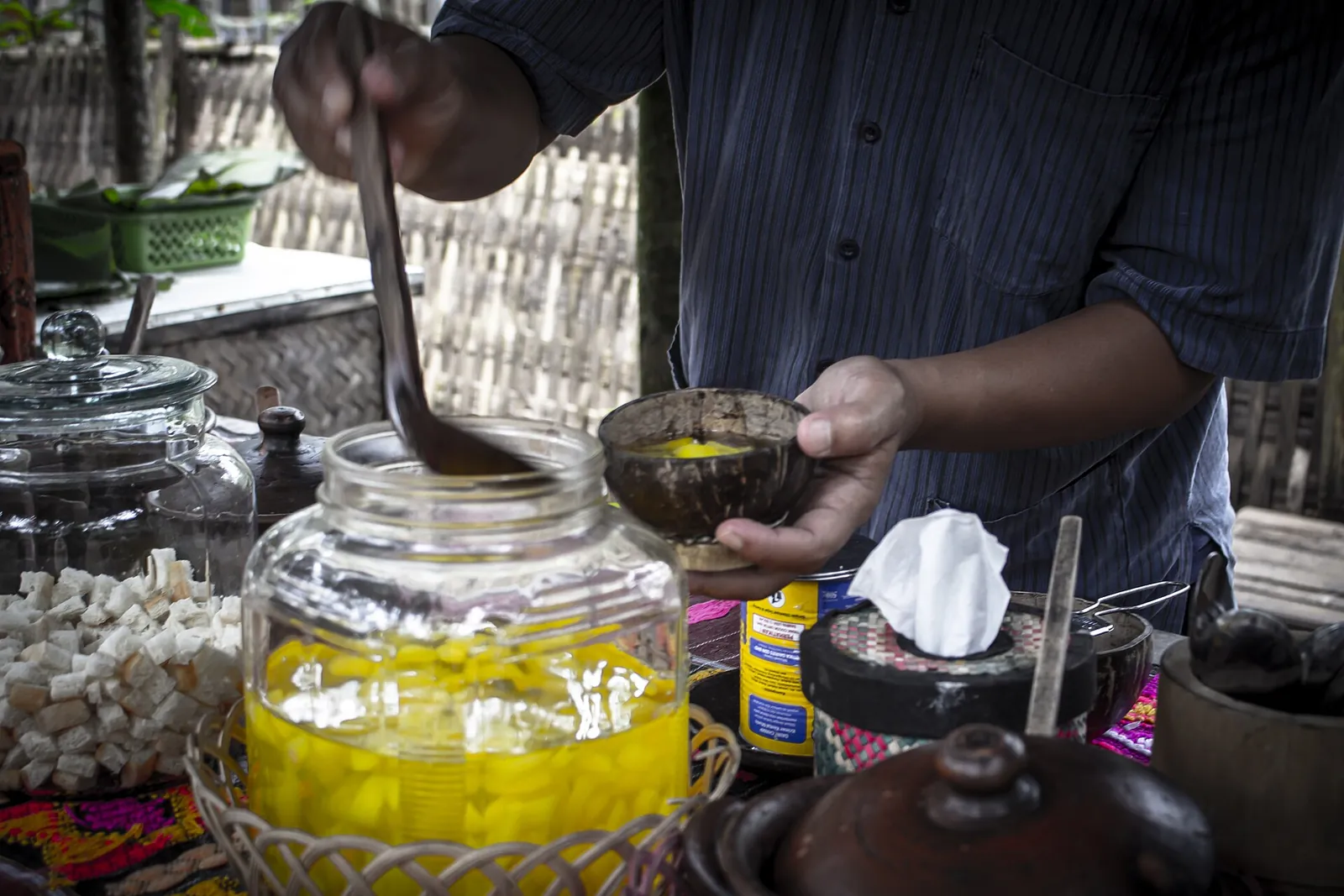 A vendor ladling pieces of carica fruit in yellow syrup from a glass jar, Dieng