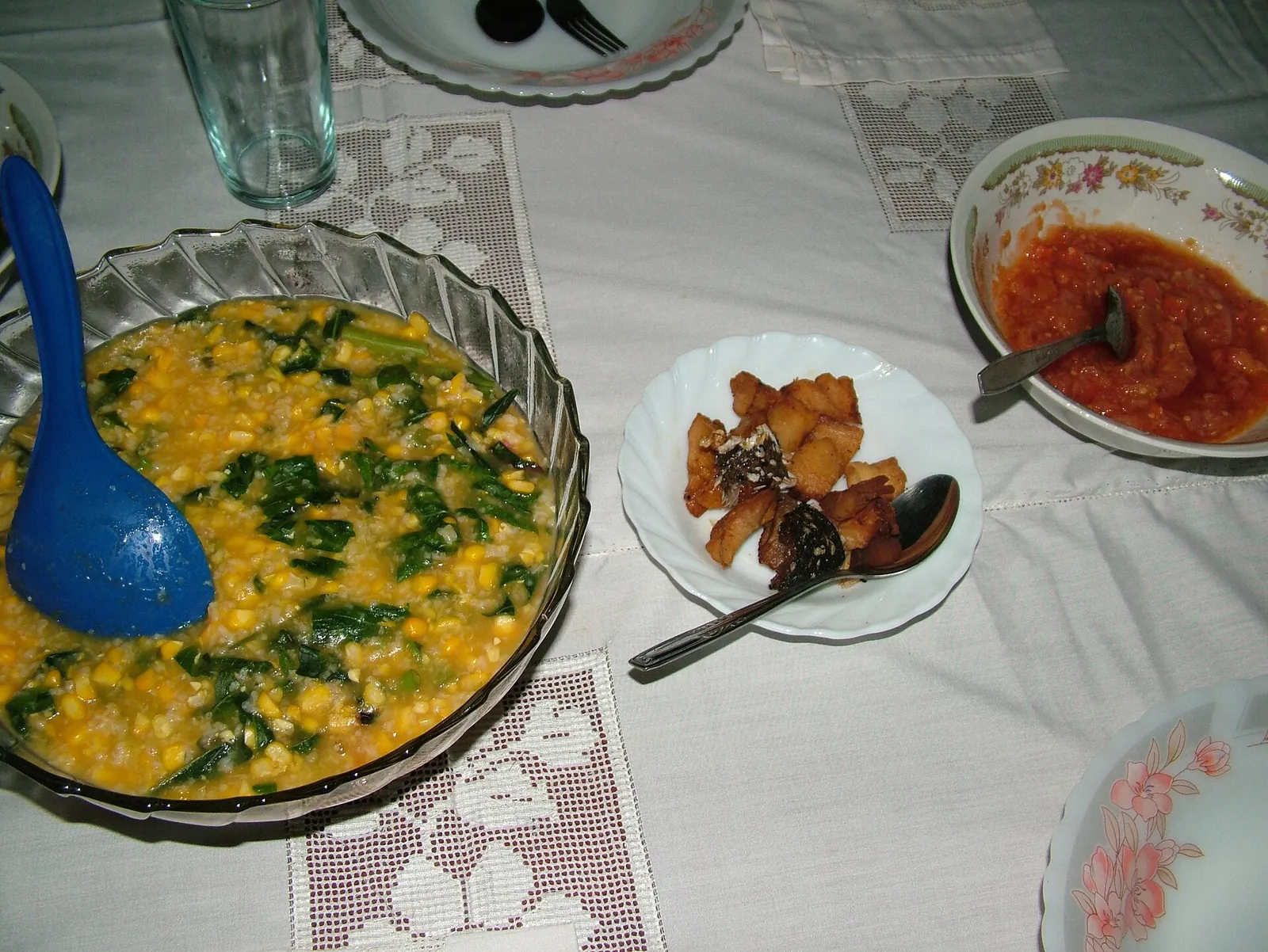 Bowl of yellow tinutuan vegetable rice porridge with side dishes of chilli sambal and fried salted fish