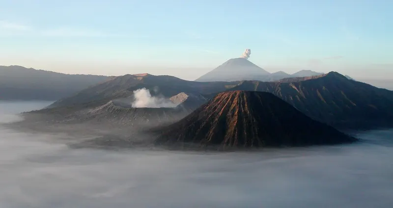 Mount Bromo smoking above a sea of morning cloud in the Tengger caldera, with Batok in front and Semeru erupting behind