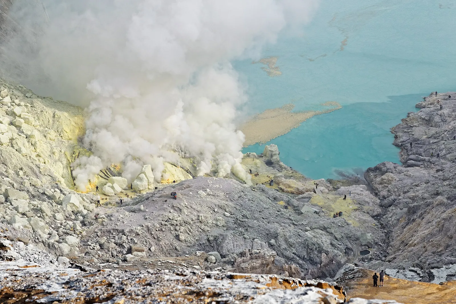 Turquoise acid lake in the Kawah Ijen crater, seen from above with sulphur smoke and the miners' path on the crater wall