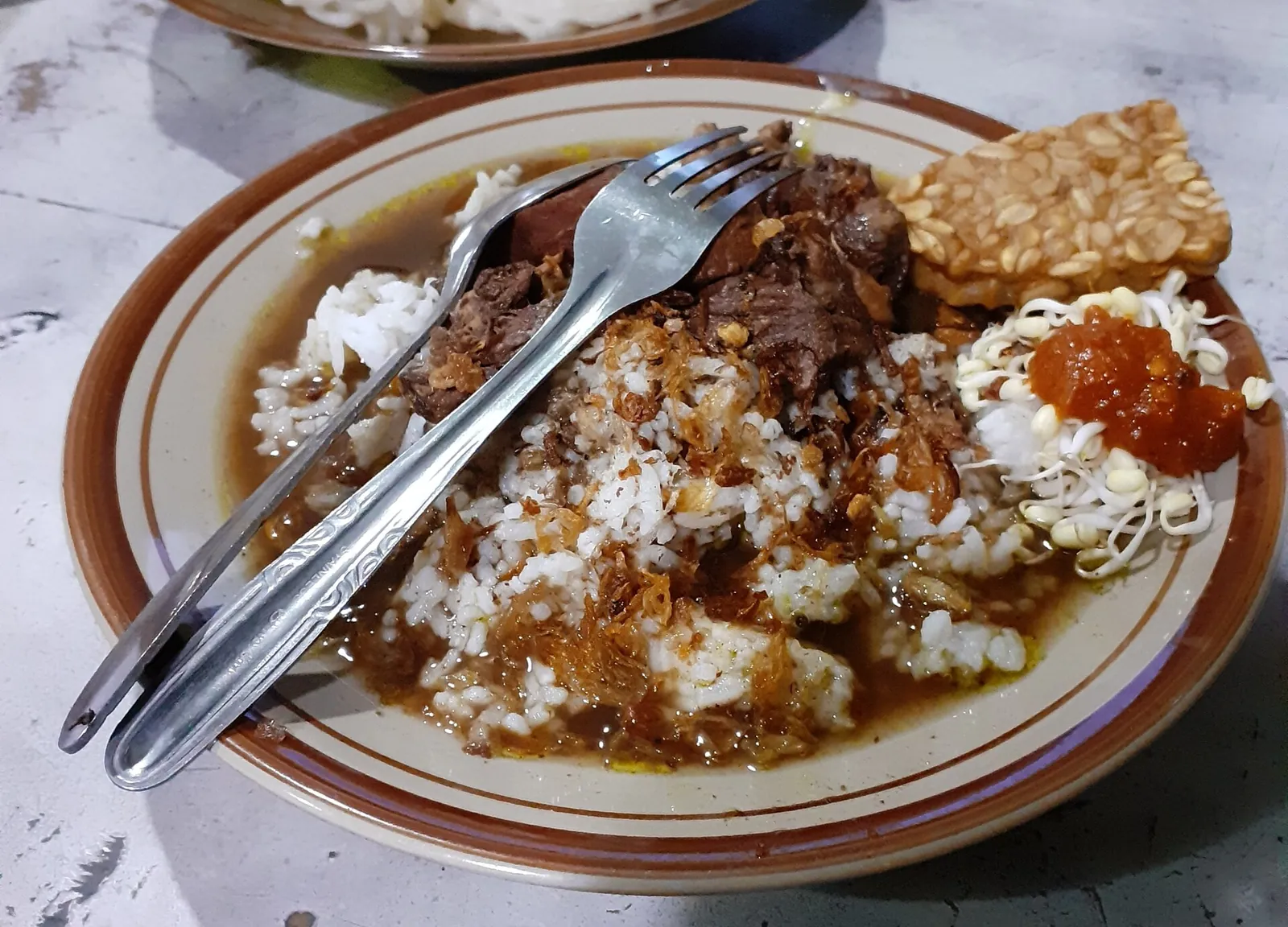 Plate of rawon, black beef soup with rice, beef, bean sprouts, sambal and a cracker