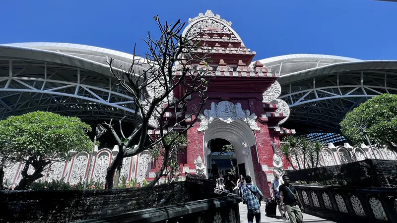 Balinese carved gate in front of the curved roofs of Ngurah Rai International Airport under a blue sky