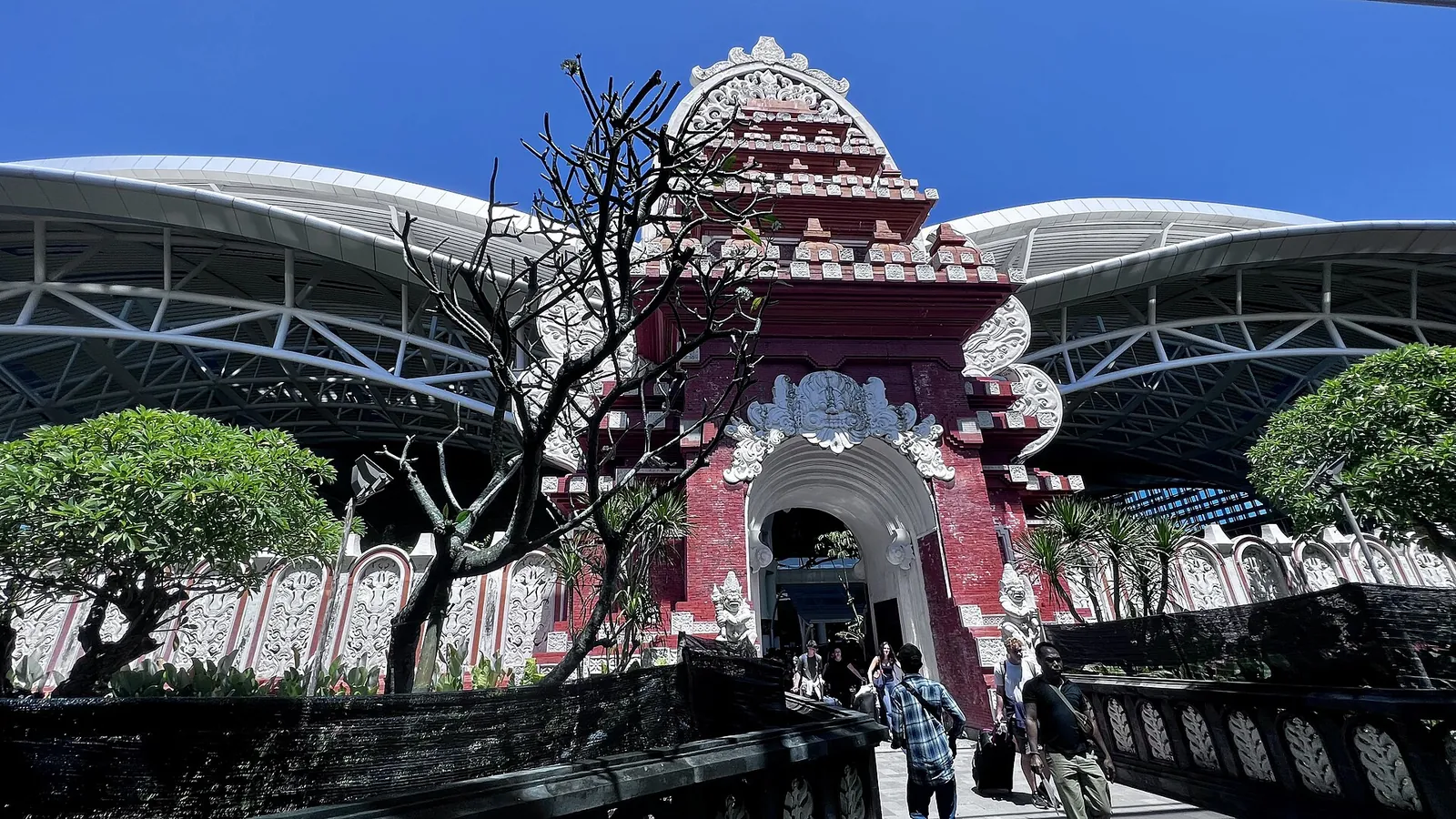 Balinese carved gate in front of the curved roofs of Ngurah Rai International Airport under a blue sky