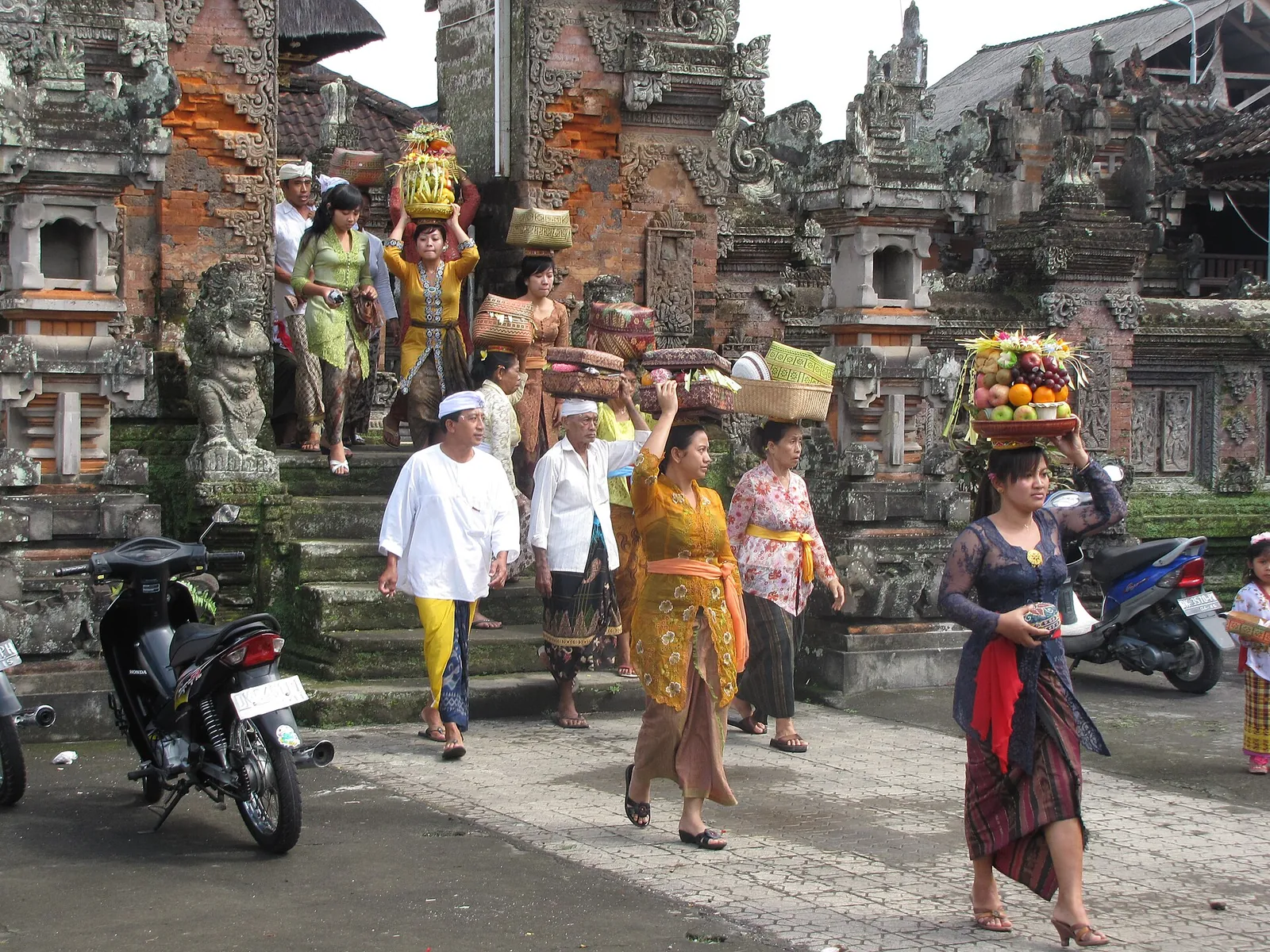 Balinese worshippers in temple dress leaving a temple with offerings carried on their heads during Kuningan
