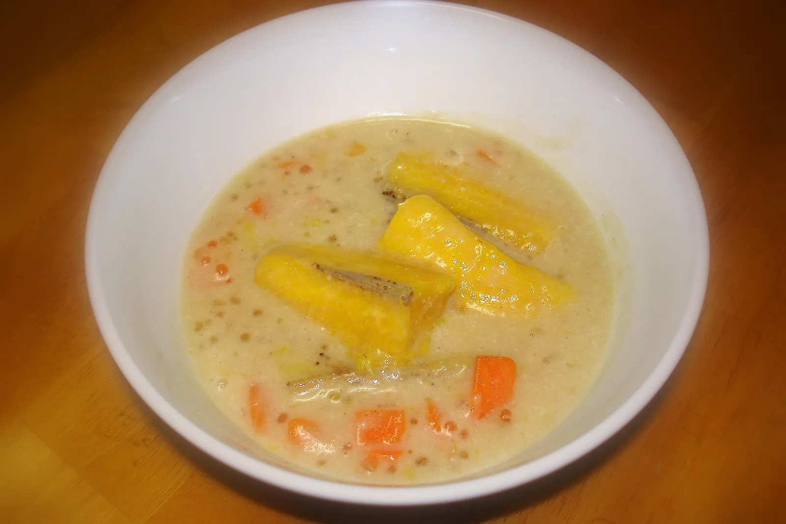 A bowl of kolak pisang: banana pieces and small orange cubes in a creamy coconut-milk broth