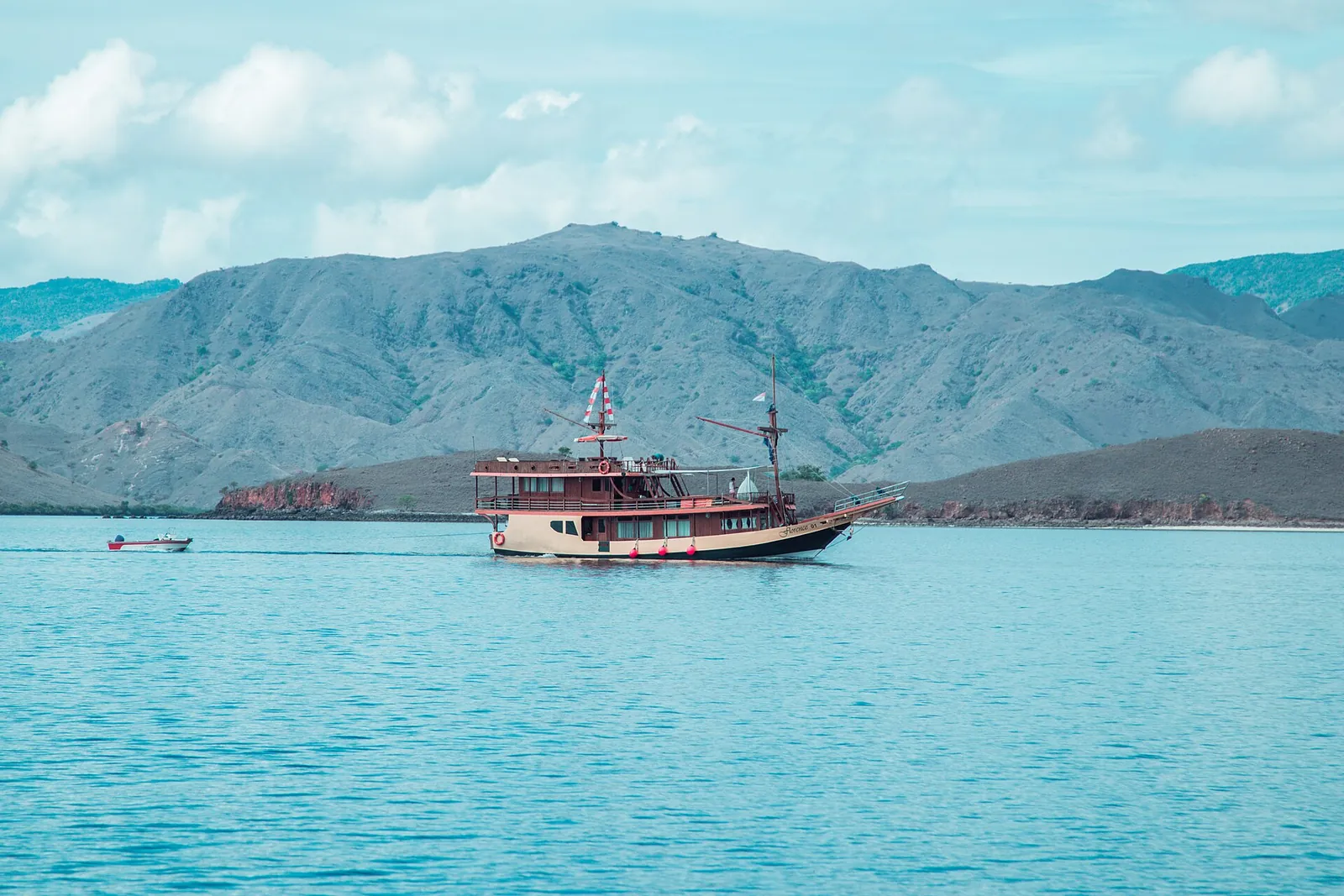 A red-and-white wooden phinisi boat on turquoise water in front of dry hills near Labuan Bajo