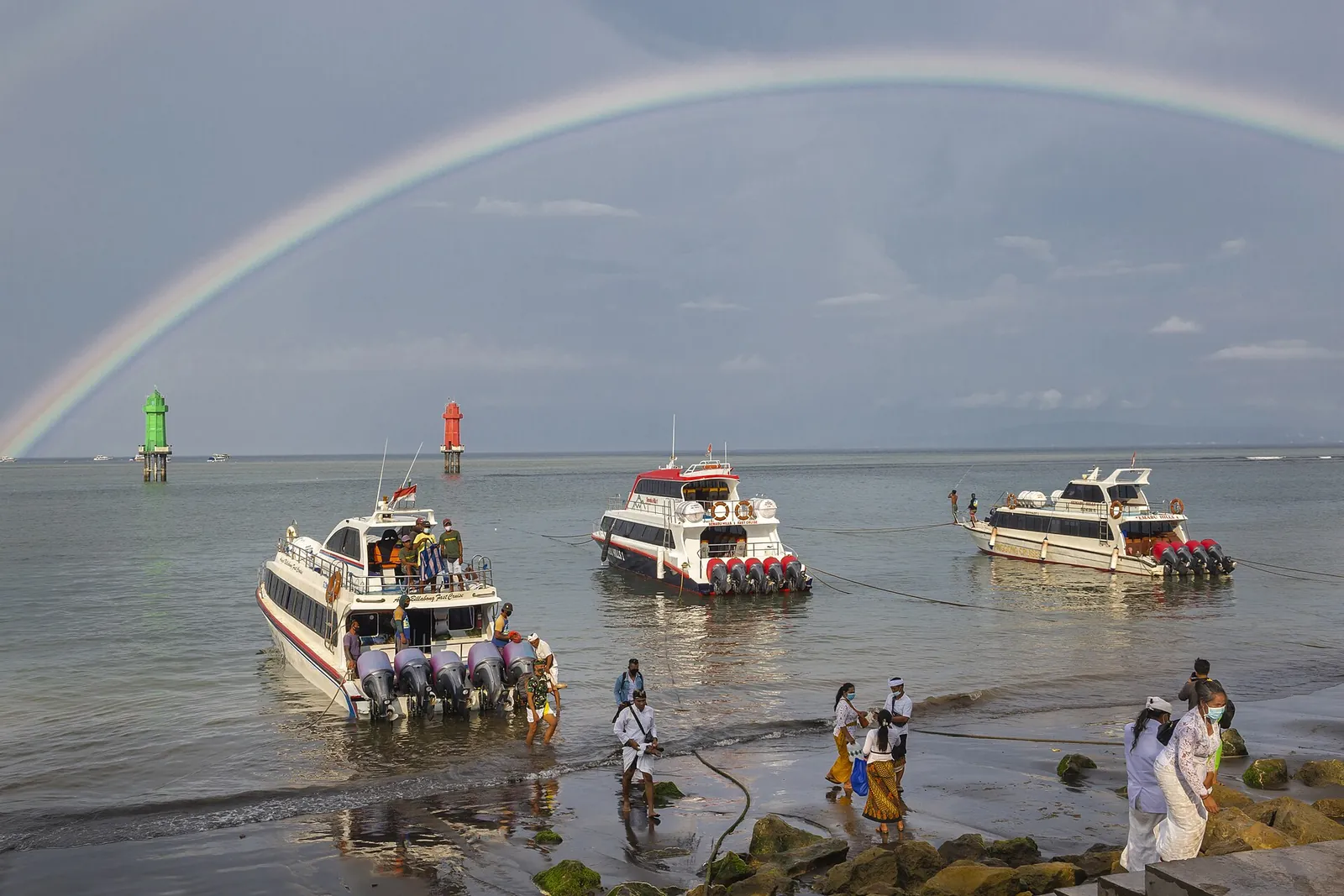 Several white fast boats in shallow water off the beach at Sanur under a rainbow