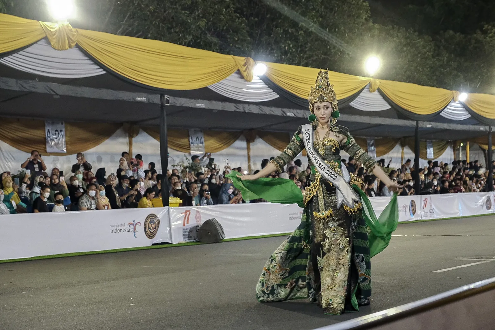 Uczestnik w misternym zielono-złotym kostiumie na trasie Jember Fashion Carnaval