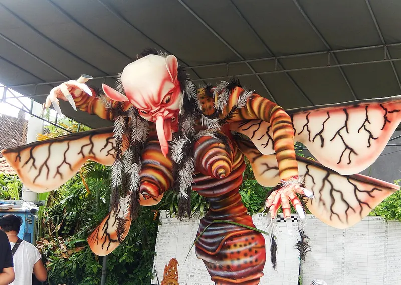 A giant winged ogoh-ogoh effigy with a tusked face standing under a canopy on a street in Ubud before the Nyepi eve parade