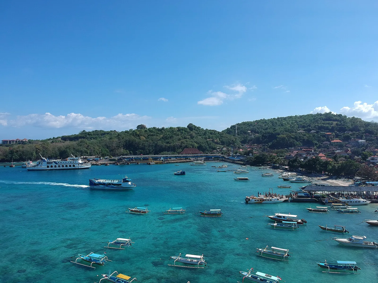 Turquoise bay at Padangbai in east Bali crowded with fast boats, ferries and fishing boats below a green hillside
