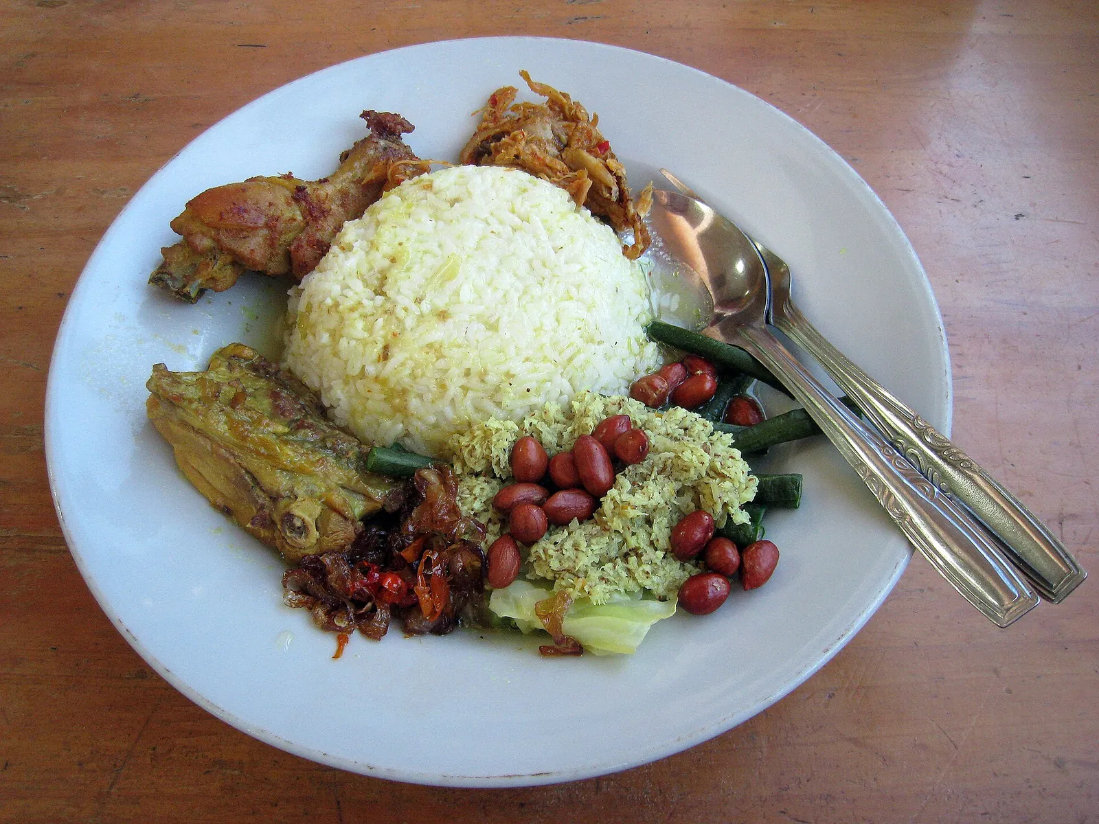 A plate of Balinese nasi campur with white rice, spiced ayam betutu chicken, peanuts, sambal and vegetables