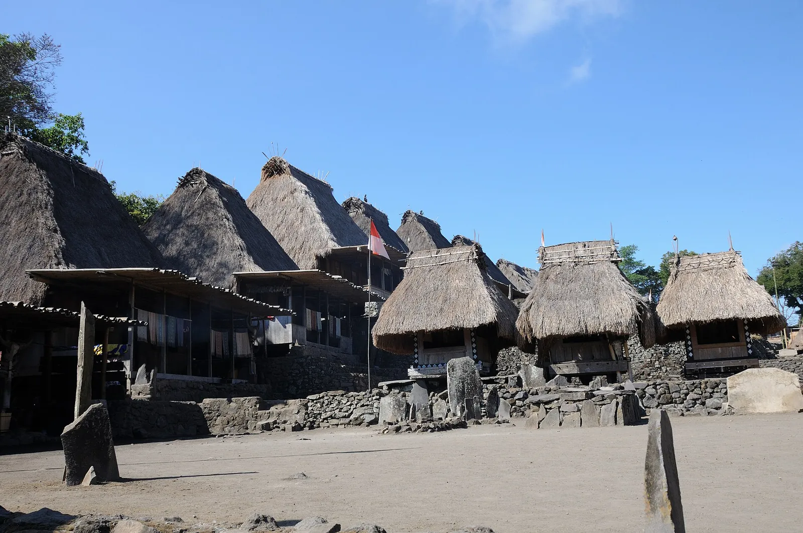 Thatched traditional houses and stone platforms around the yard of Bena village under a clear sky