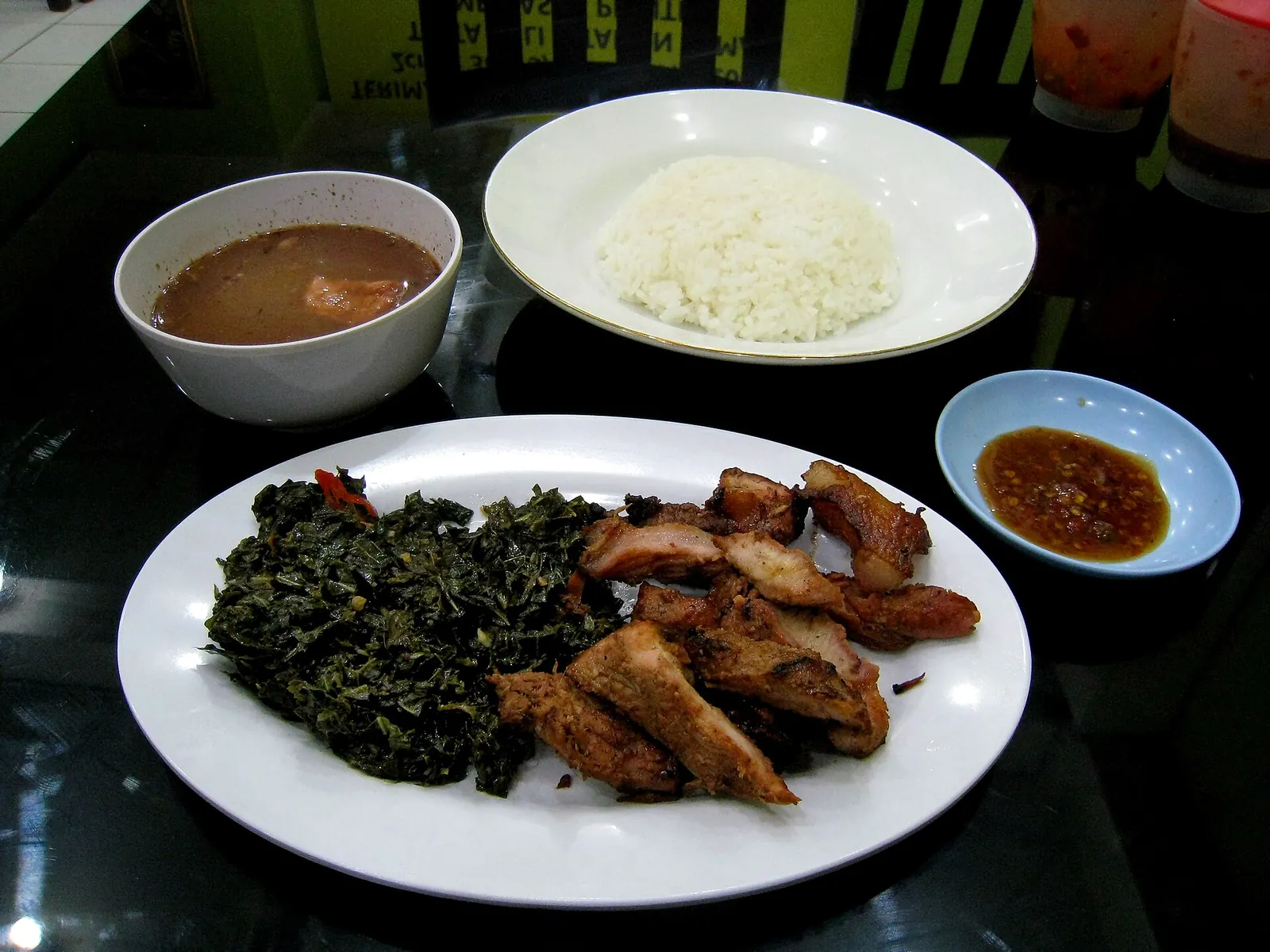 A plate of sliced smoked pork with greens, a bowl of soup, steamed rice and a dish of red sambal