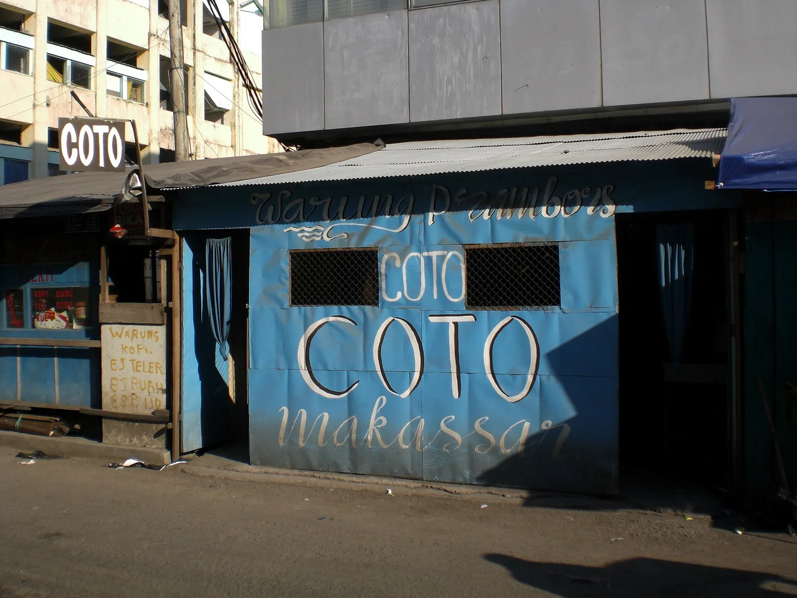 A small blue roadside warung painted with the words Coto Makassar
