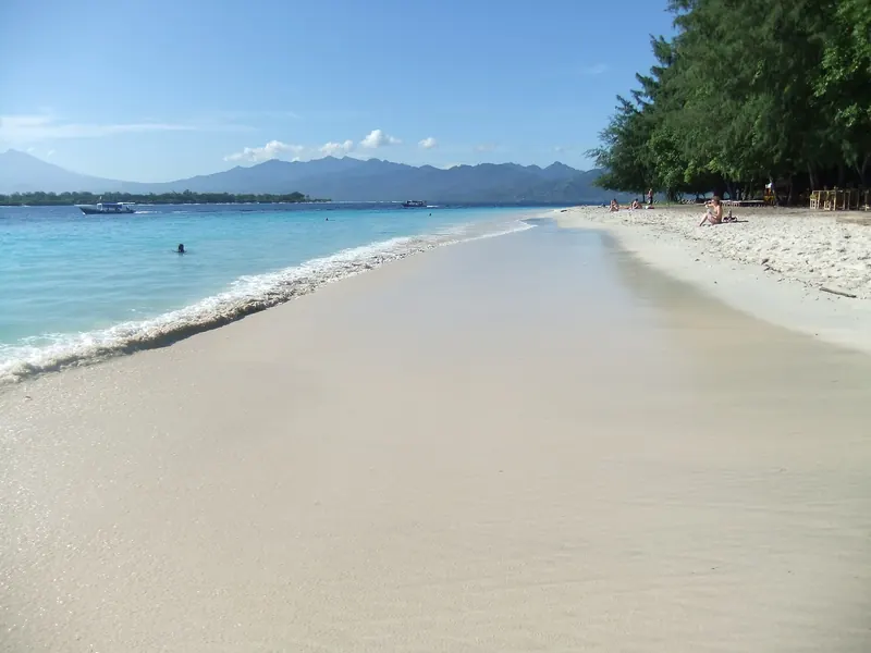 A long white sand beach on Gili Trawangan with turquoise water and mountains on the horizon