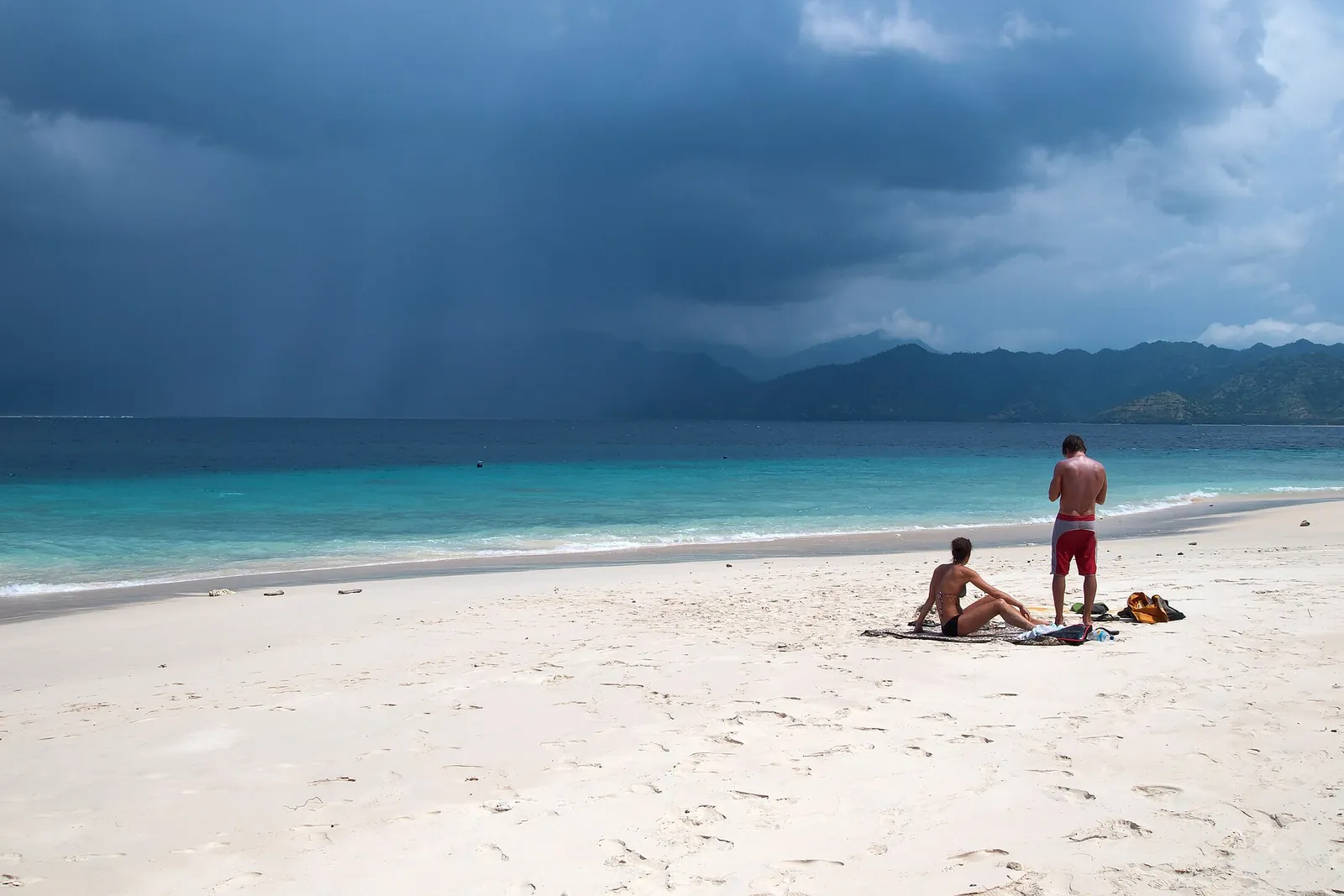 Two people on a white sand beach on Gili Meno under a cloudy sky