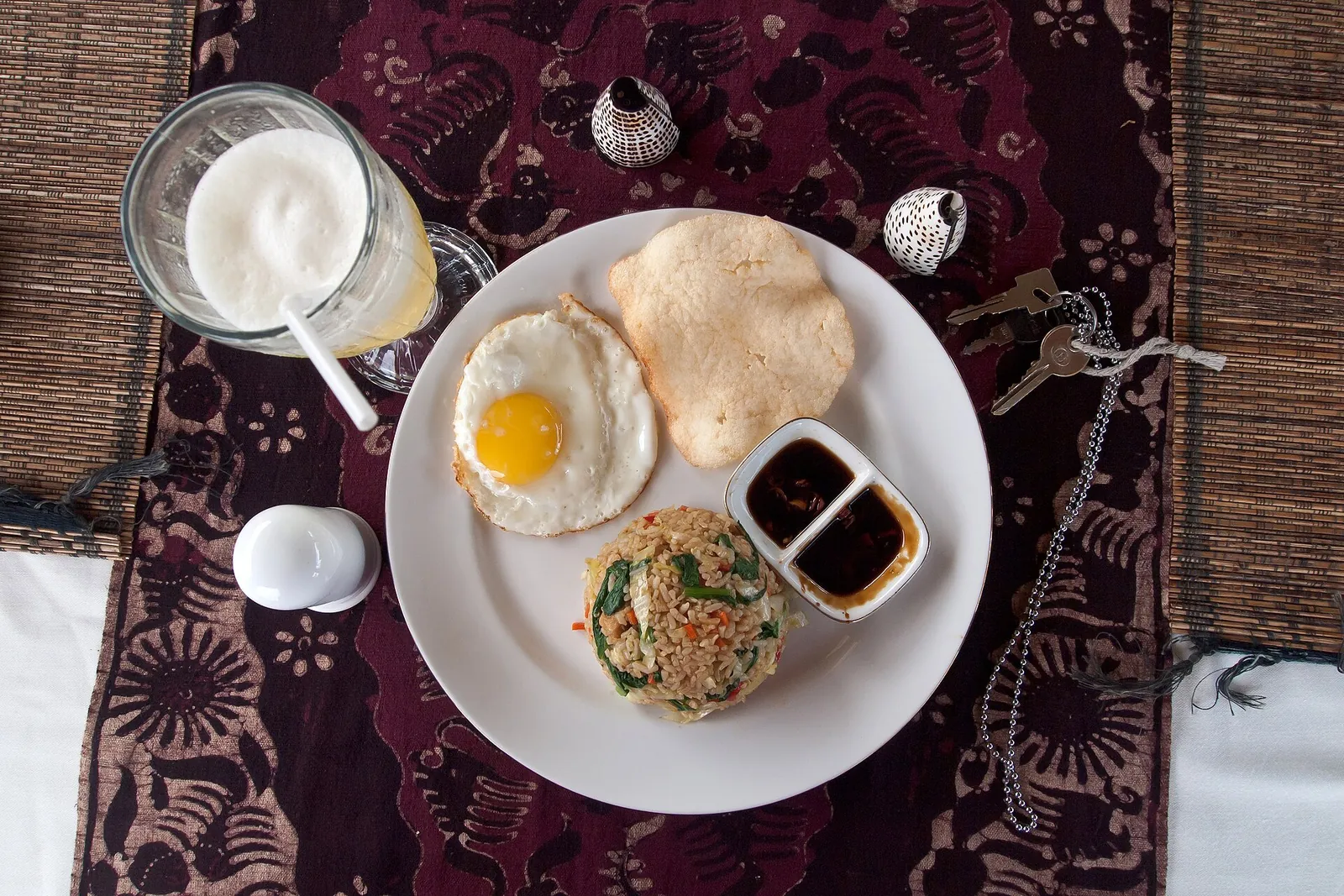 A plate of nasi goreng with a fried egg, a prawn cracker and small dishes of sauce, beside a glass of juice, on Gili Trawangan