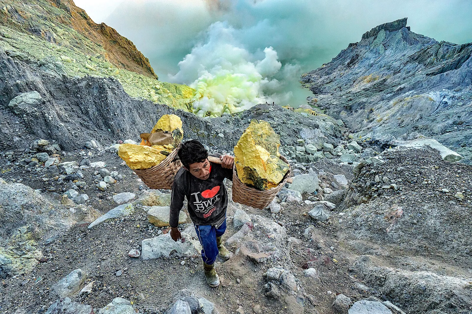A sulphur miner carrying two baskets of yellow sulphur up a rocky path inside Kawah Ijen