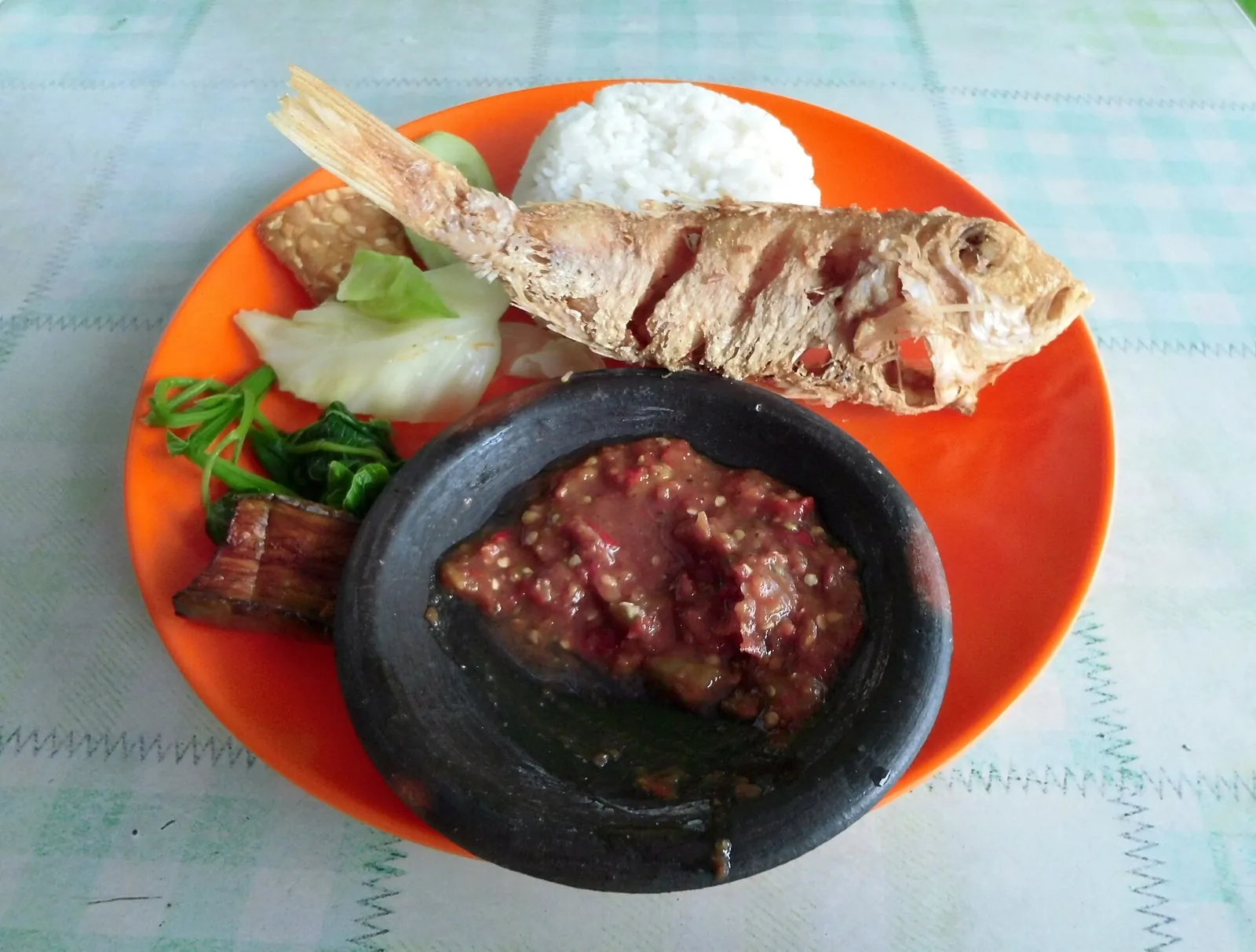 Nasi tempong on an orange plate: rice, fried fish, fried tofu and tempeh, boiled greens and a bowl of red sambal