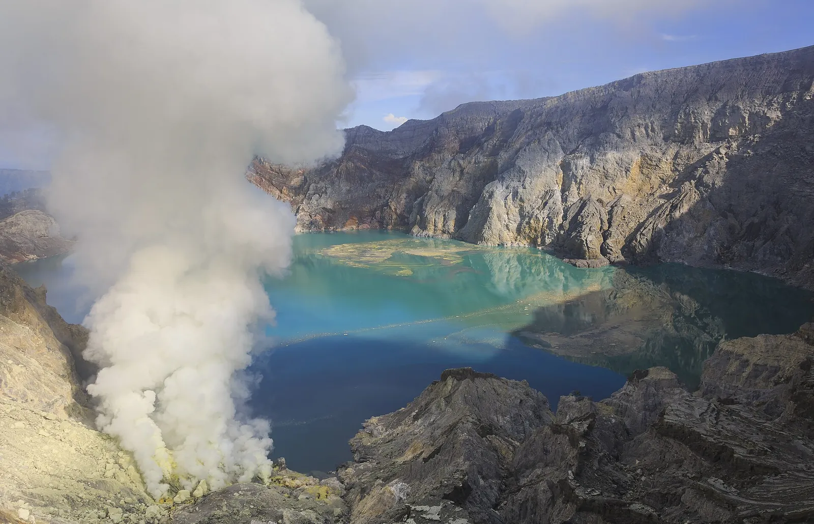 Sulphur smoke rising beside the turquoise acid lake inside the Kawah Ijen crater