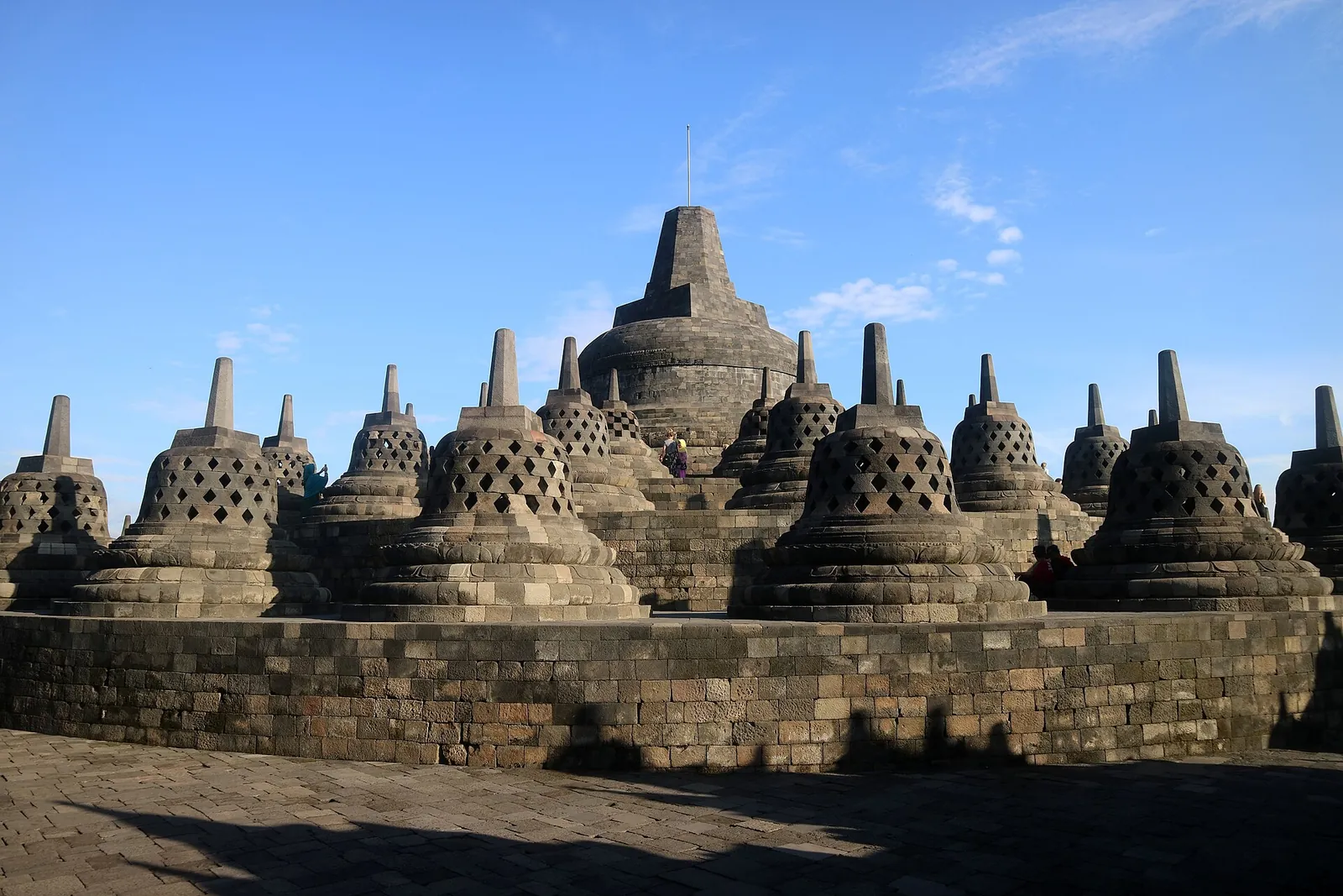 Rows of bell-shaped stupas around the main stupa on Borobudur's upper terrace under a blue sky