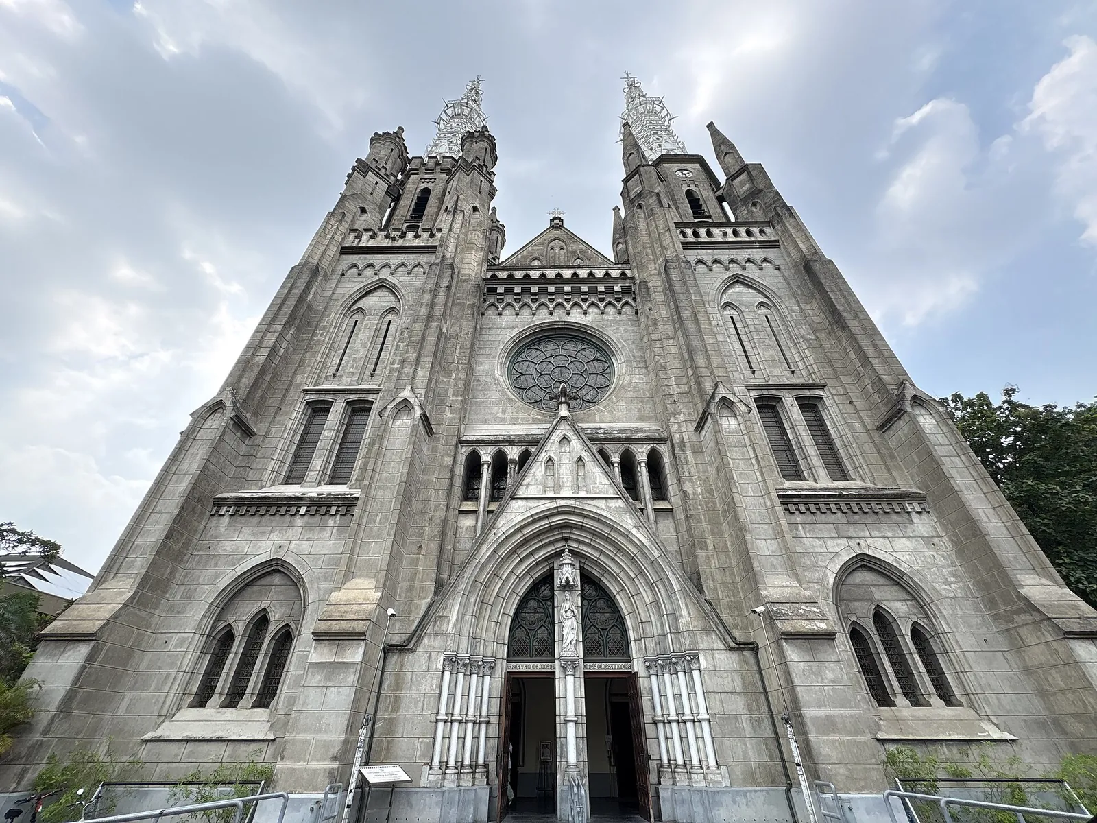 The neo-Gothic grey facade and twin spires of Jakarta Cathedral against a cloudy sky