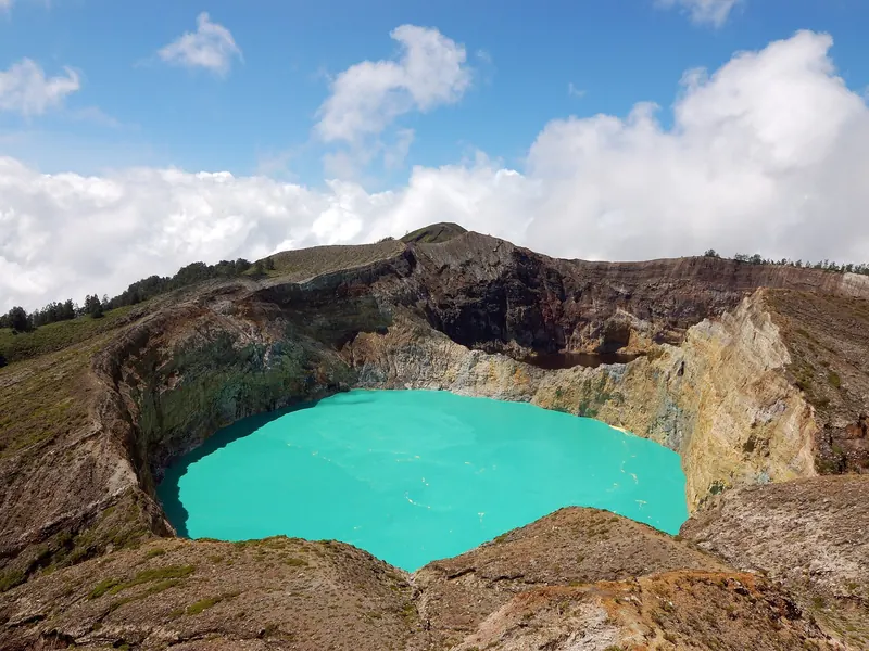 A turquoise crater lake inside steep, rust-coloured crater walls at Kelimutu under a blue sky