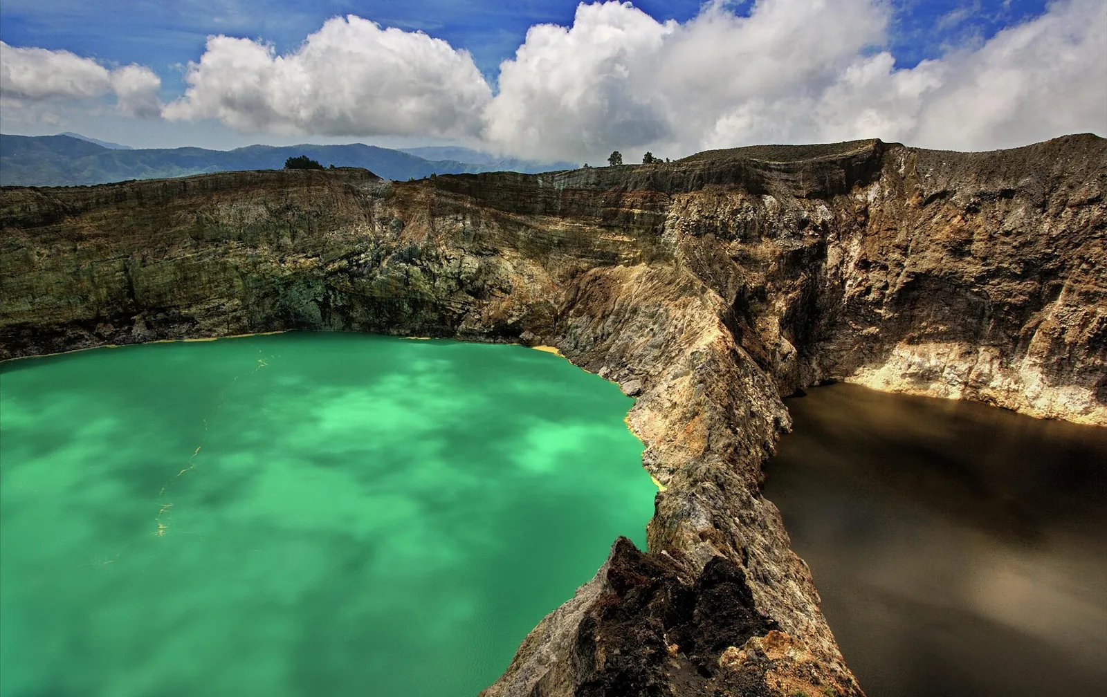 A bright green crater lake beside a dark lake, separated by a narrow crater wall, at Kelimutu
