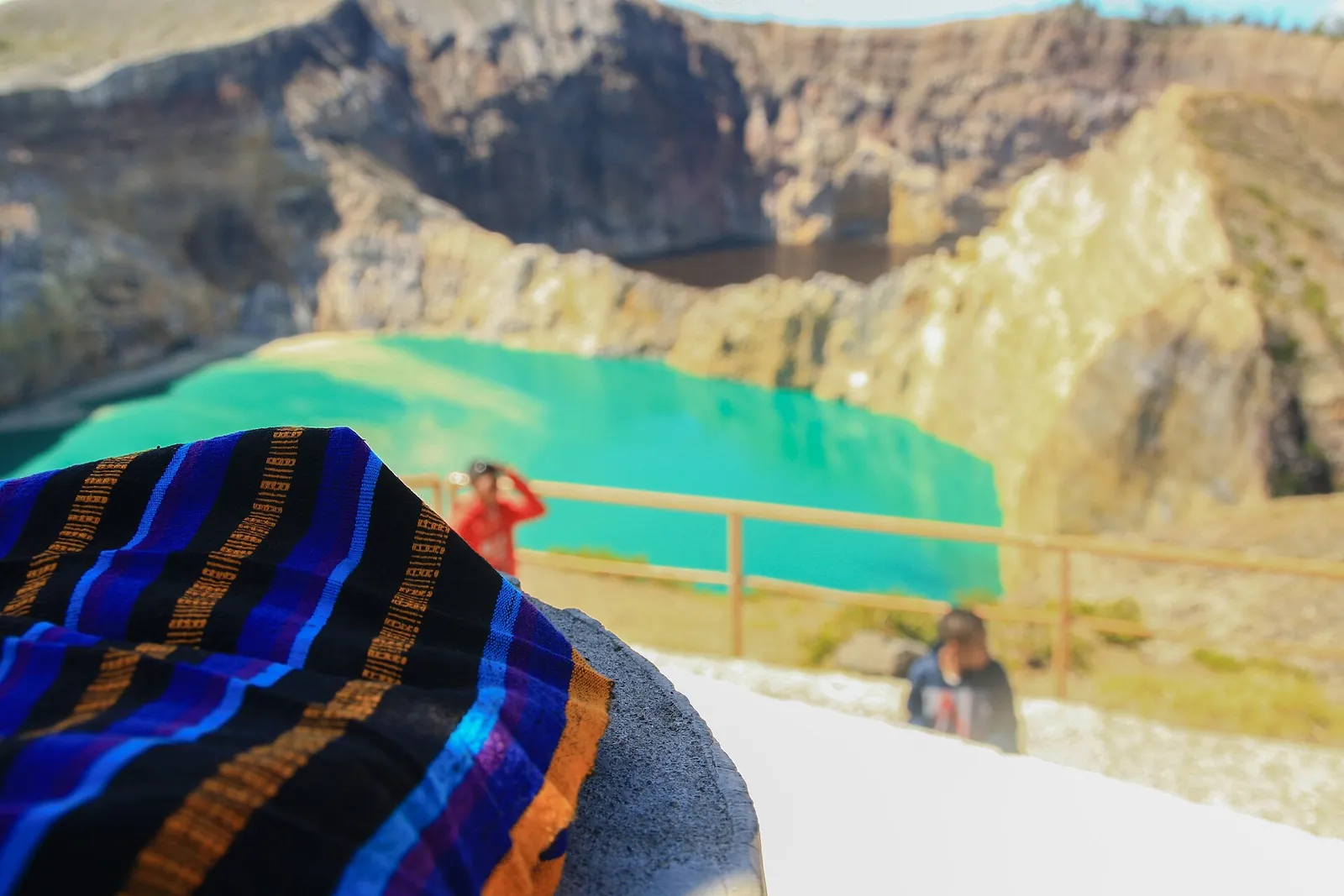 A striped Lio ikat cloth laid out for sale at the Kelimutu lakes viewpoint, with a turquoise lake behind