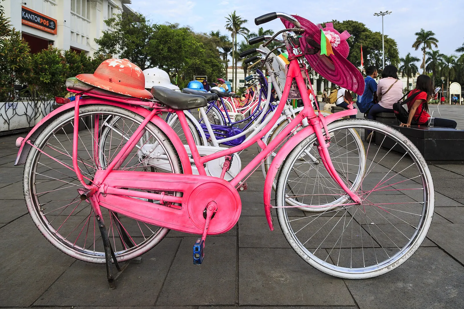 Pastel-painted rental bicycles with matching sun hats lined up on Fatahillah Square