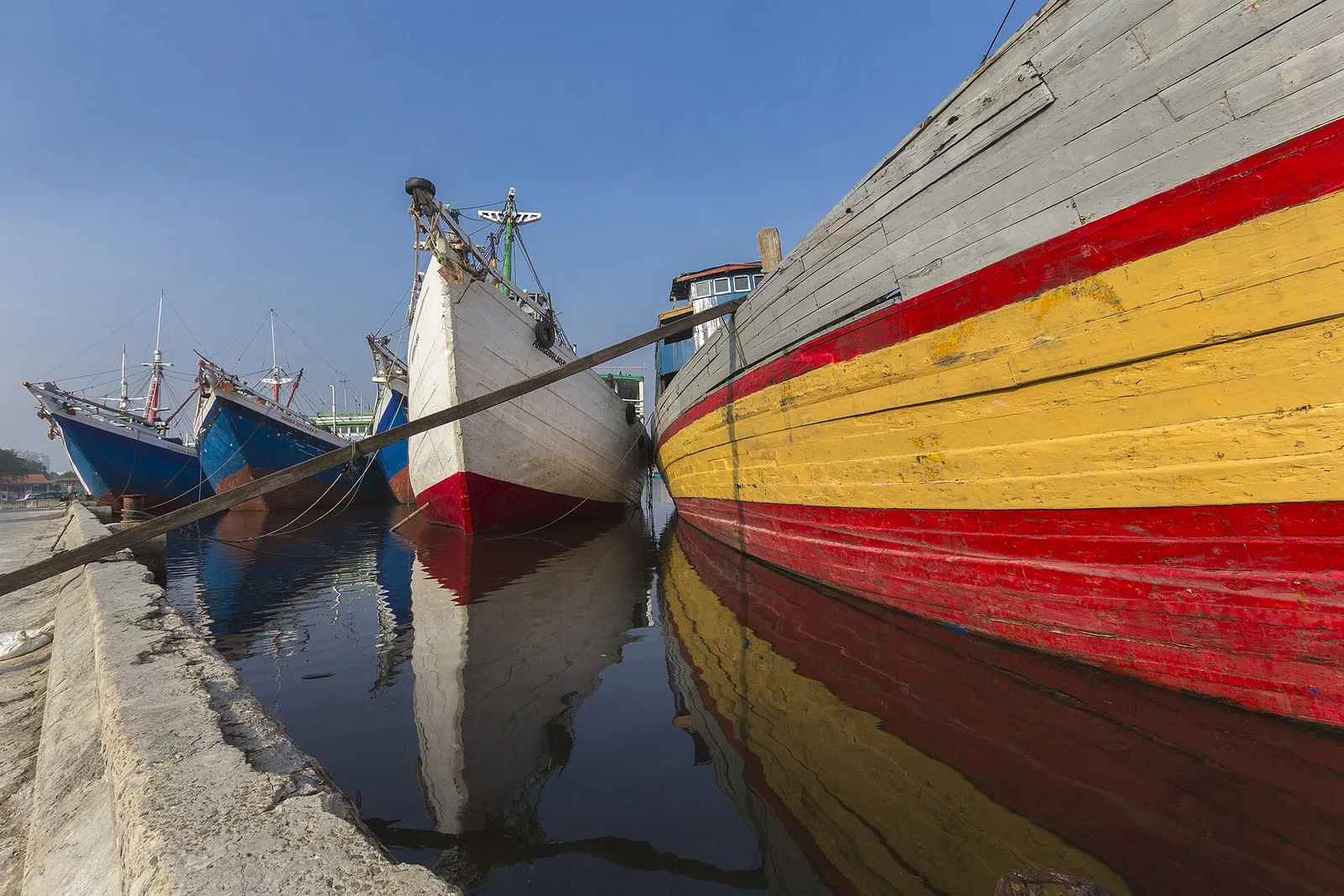 Wooden pinisi cargo ships with red and yellow painted hulls moored side by side at Sunda Kelapa harbour