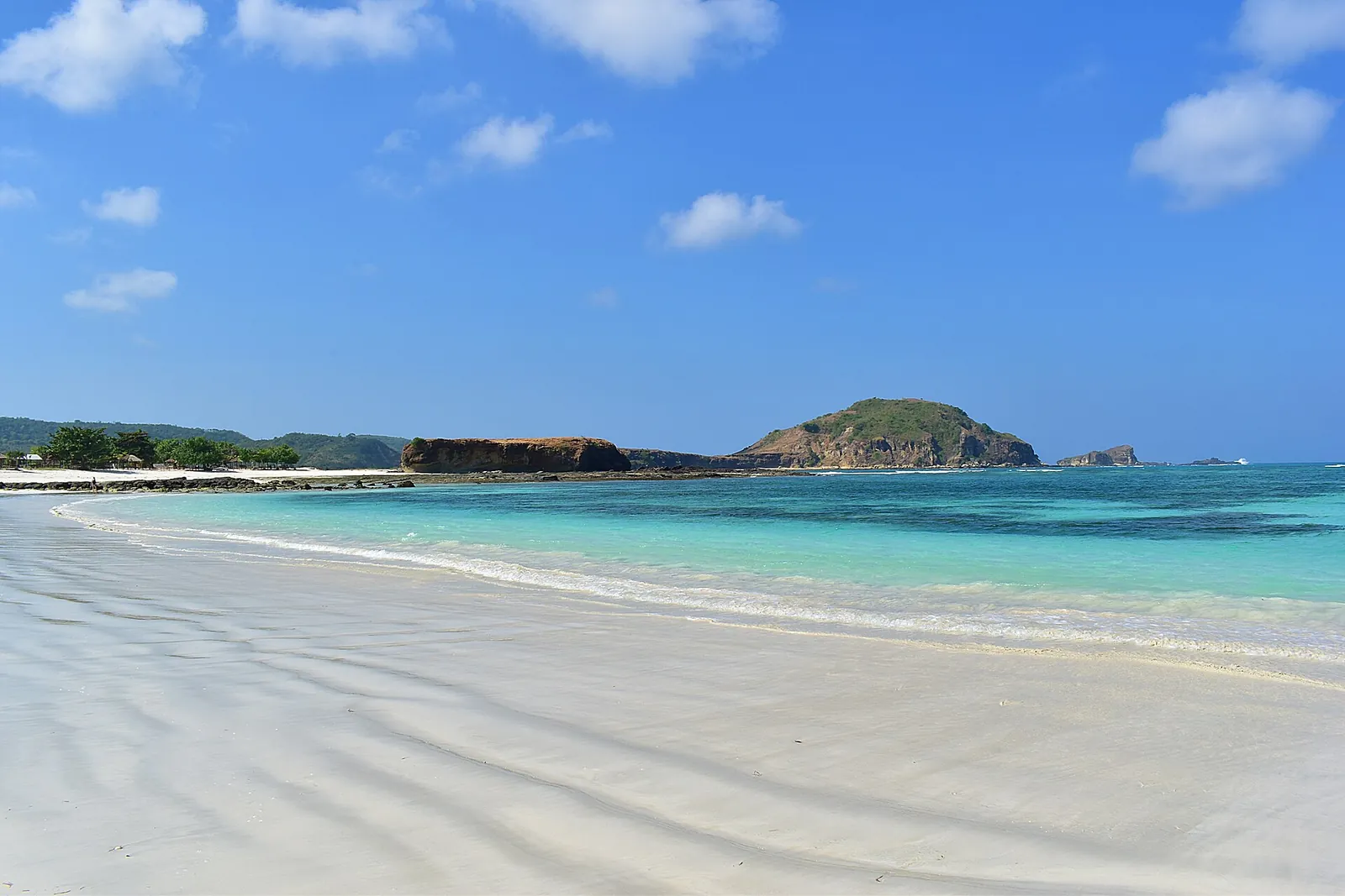 Wide white-sand beach with clear turquoise water and green headlands at Tanjung Aan, south Lombok