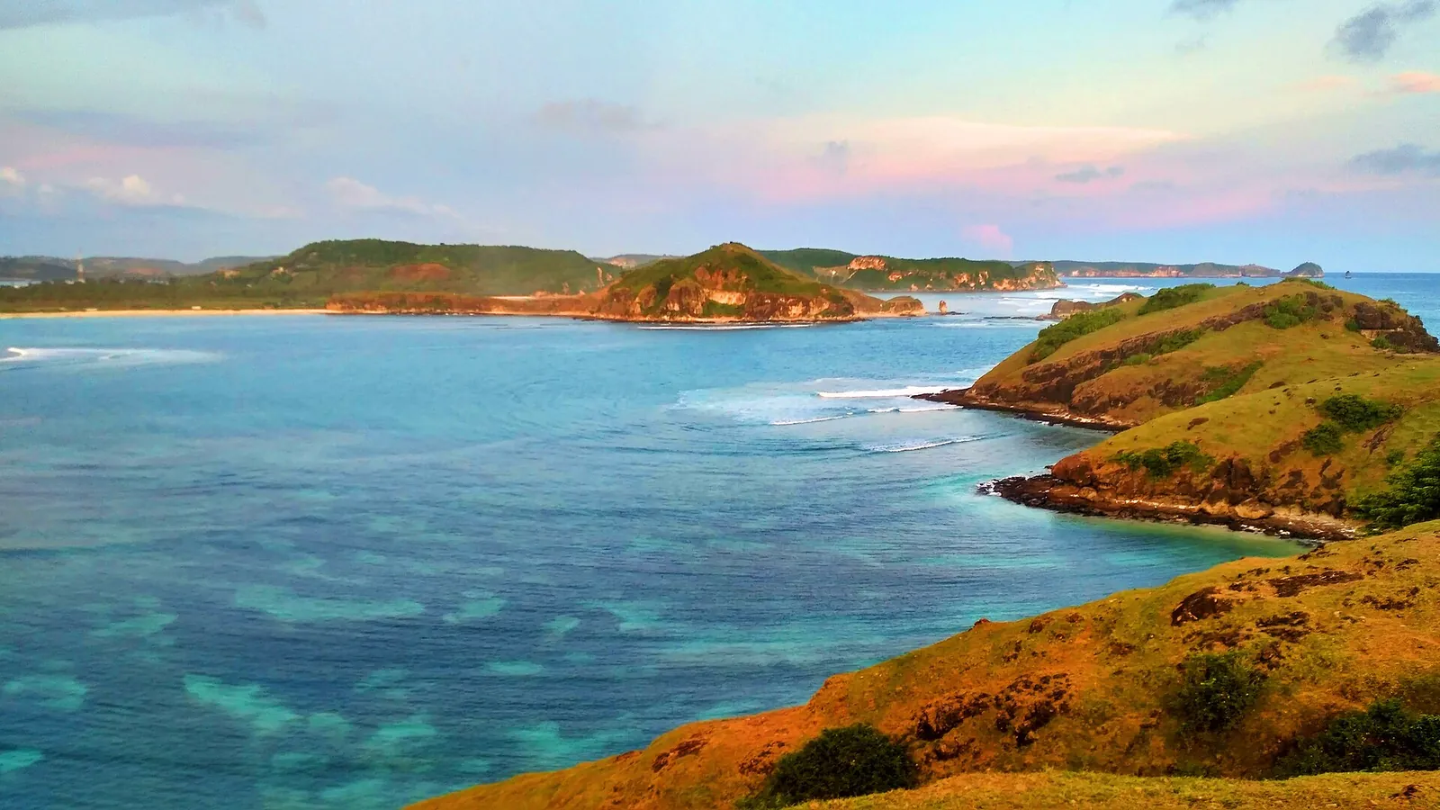 View from a grassy headland over turquoise bays and green hills at Tanjung Aan, Lombok