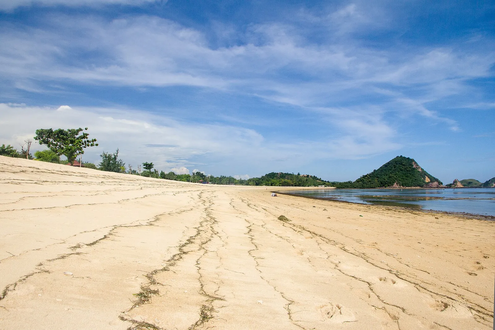 Sandy beach with a green hill and calm water at Kuta Beach, Lombok