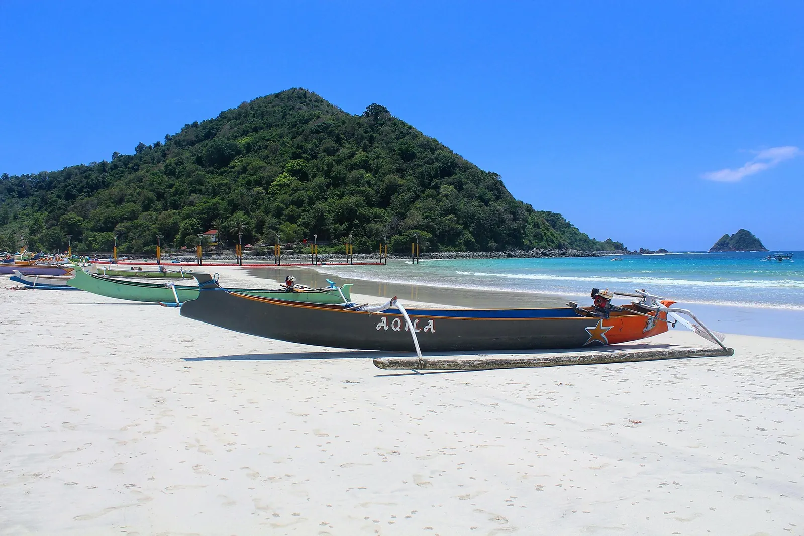Outrigger fishing boats on white sand below a green hill at Selong Belanak, Lombok