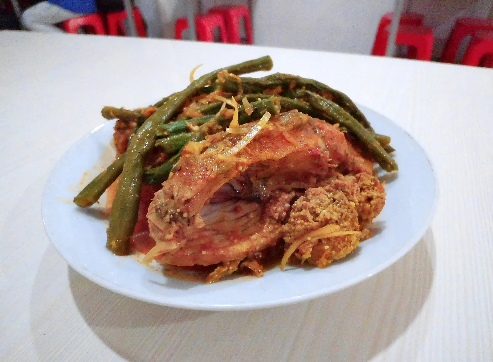 Plate of arsik, carp in a red-orange spice sauce topped with long beans