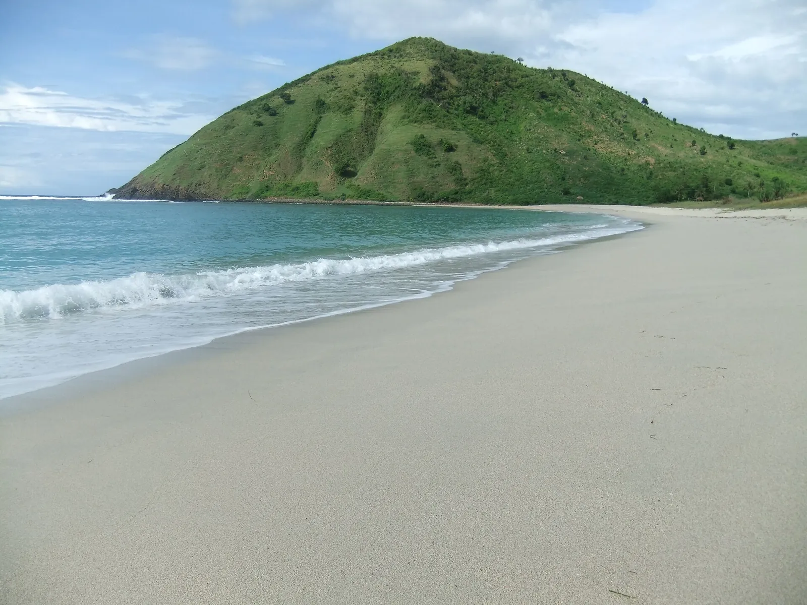 White-sand curve of Mawun Beach on Lombok's south coast, with a green hill rising behind the bay