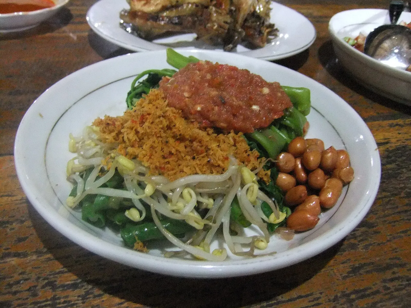 Plate of plecing kangkung: water spinach and bean sprouts topped with red tomato sambal, fried peanuts and coconut flakes