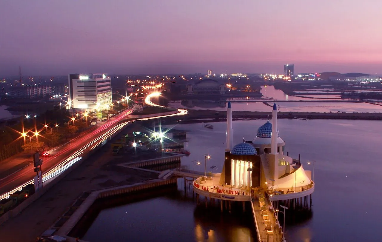 The floating Amirul Mukminin Mosque with its blue domes on the water at Losari, Makassar, at dusk with city lights behind