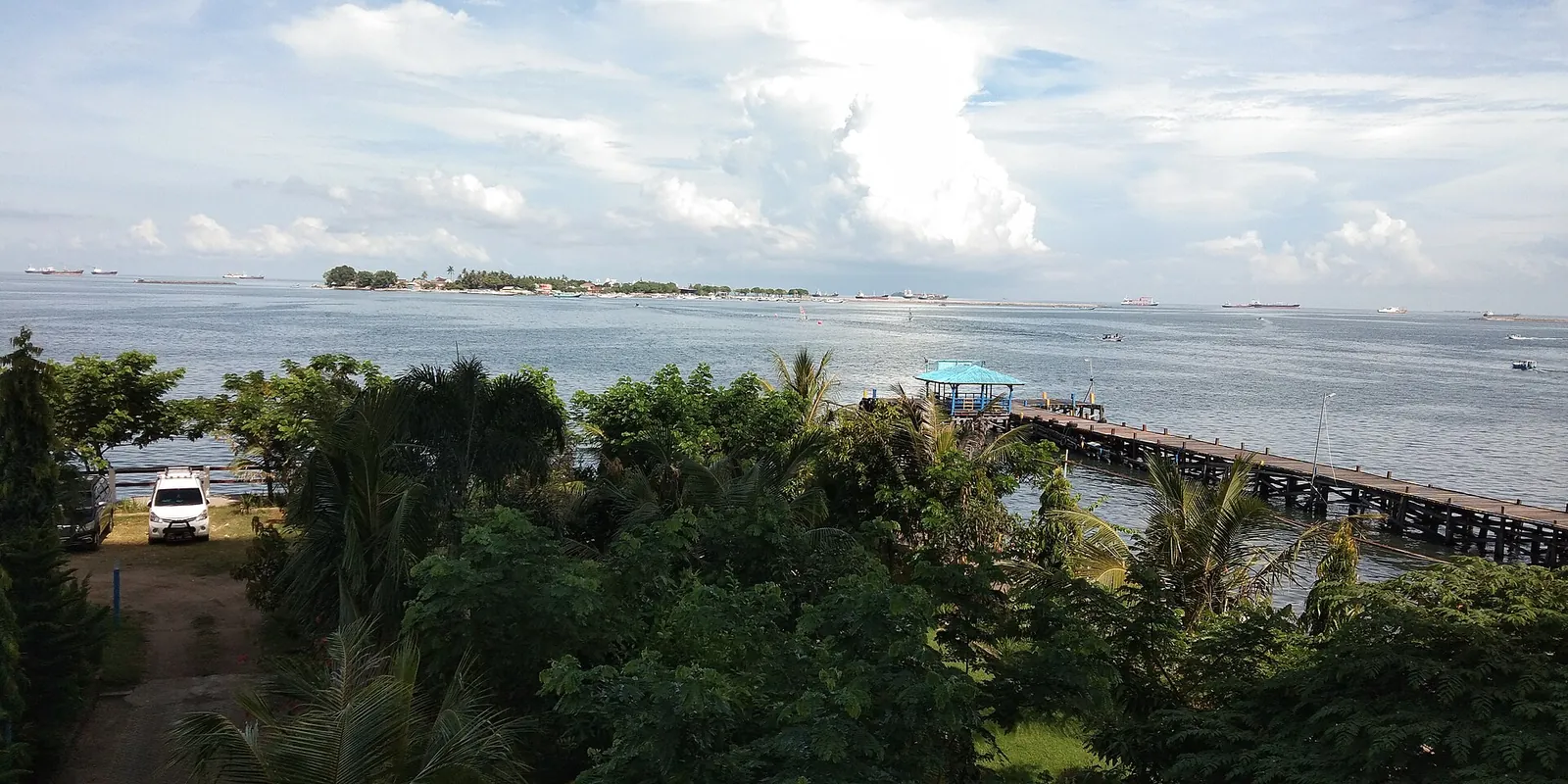 Morning view over Losari Beach in Makassar, with trees, a pier and the sea with small islands on the horizon