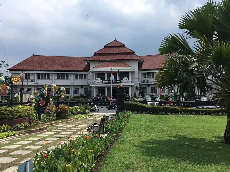 Malang town hall, a white colonial-era building with a red-tiled roof, behind a garden path lined with flowers