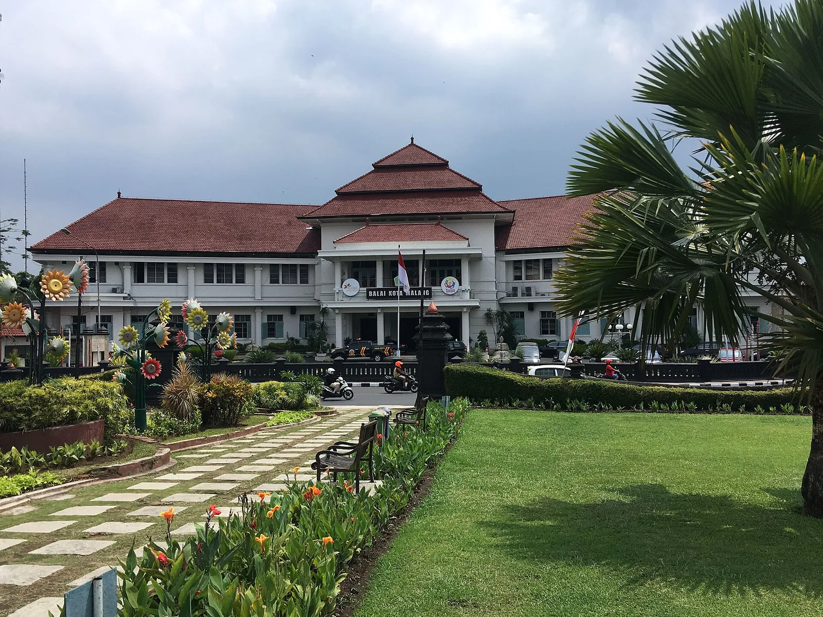 Malang town hall, a white colonial-era building with a red-tiled roof, behind a garden path lined with flowers