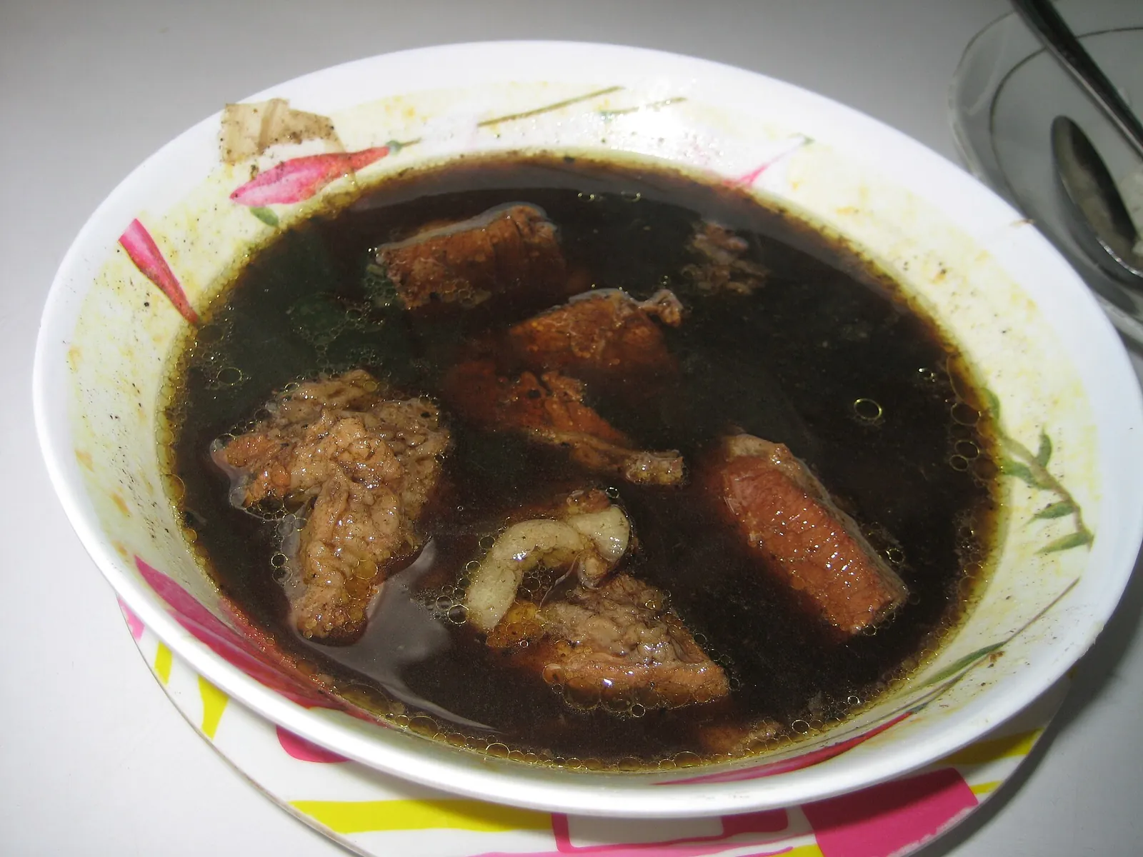 A bowl of rawon, a black beef soup, with chunks of beef in a dark broth