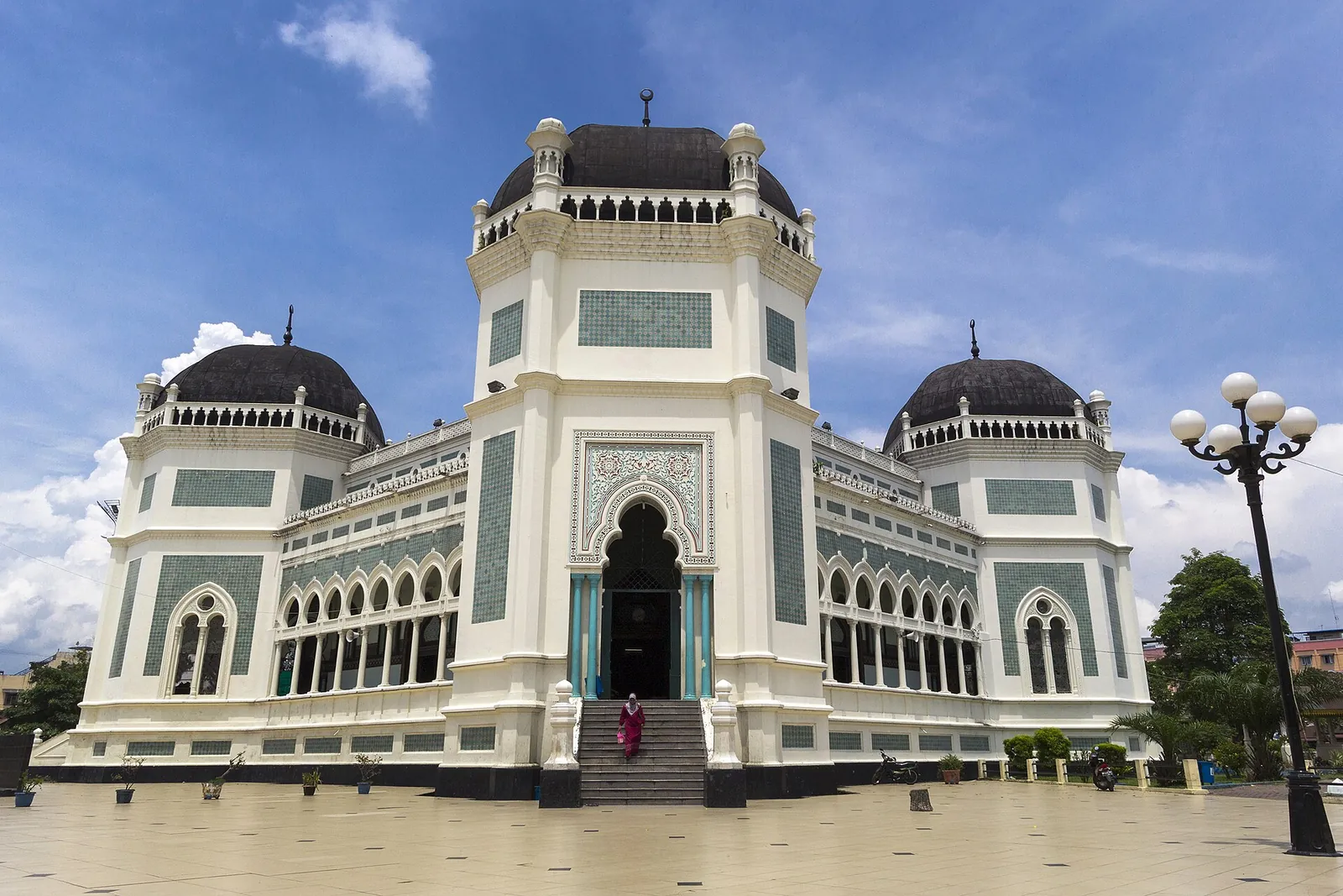 White and green Grand Mosque of Medan with black domes and a grand entrance under a blue sky