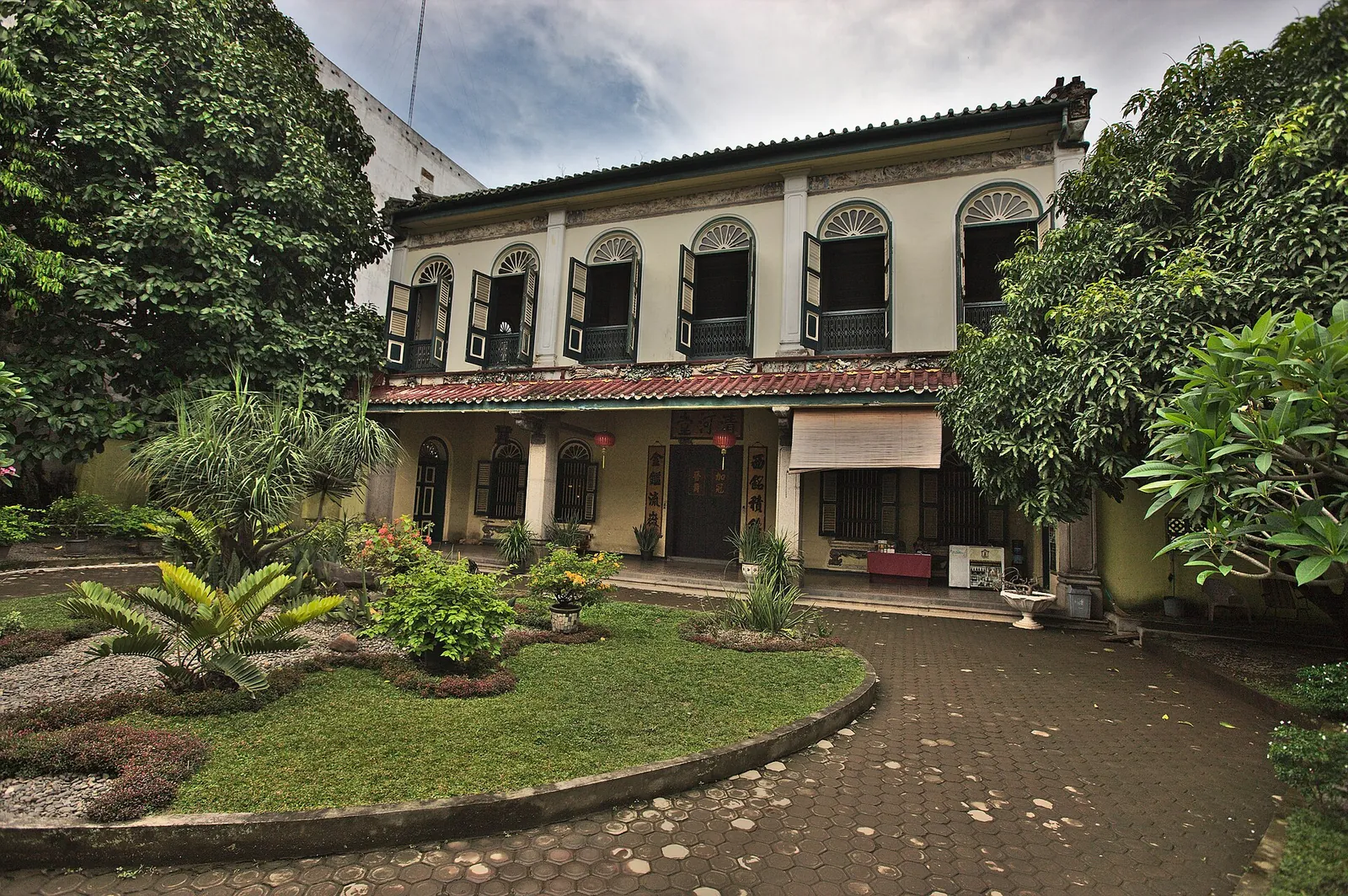 Two-storey Tjong A Fie Mansion with arched green-shuttered windows behind a garden courtyard on Jalan Ahmad Yani